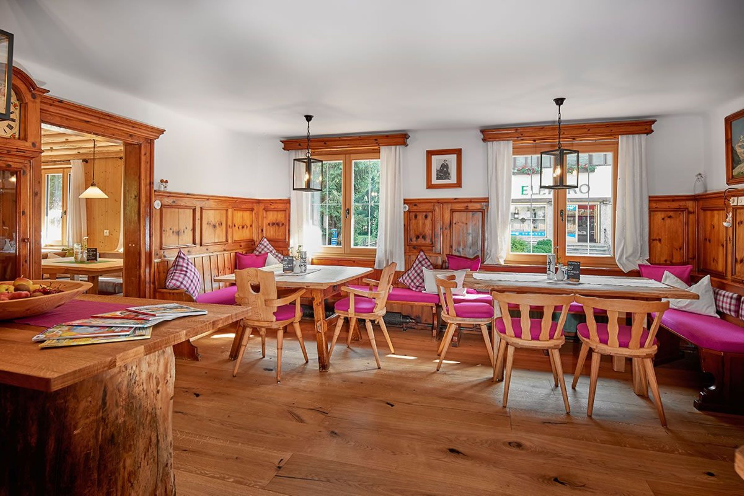 A spacious kitchen with wooden cabinets, a dining area with wooden tables and chairs, and large windows allowing natural light.