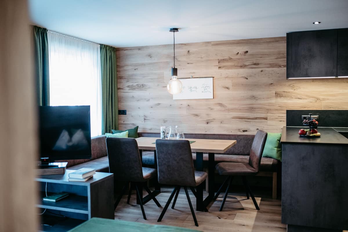 Un salon moderne avec un mur en bois, un coin repas avec une table et des chaises, un téléviseur à écran plat et un comptoir de cuisine agrémenté de fruits.