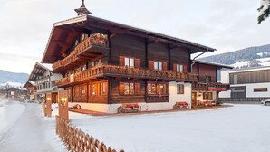 Una cabaña de madera tradicional con balcones, una zona de estar cubierta al aire libre y una calle nevada.