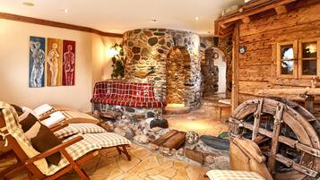 Cozy seating area with a stone fireplace, wooden rocking chairs, and a large wooden wheel.