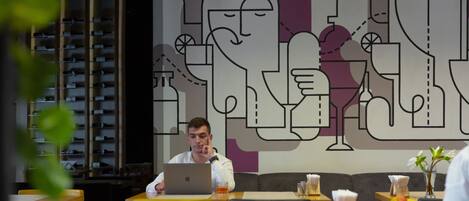 A modern restaurant interior with a large abstract mural on the wall, wooden tables, and yellow chairs.
