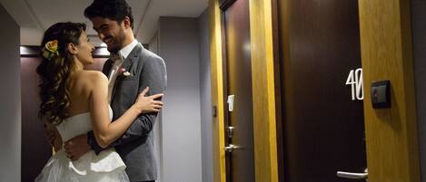 A couple embracing in a hotel corridor with wooden doors and a visible room number.