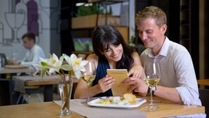 A couple dining at a restaurant with a modern interior, including a wine glass on the table and a menu. - Nova Hotel Yerevan (Yerevan)