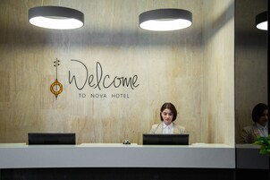 Een receptiebalie bij Hotel Nova, met een 'Welcome'-bord en twee receptionisten.