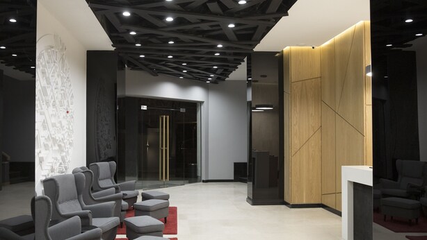A modern lobby with grey upholstered seating, a wooden accent wall, and a glass door entrance. - Nova Hotel Yerevan (Yerevan)