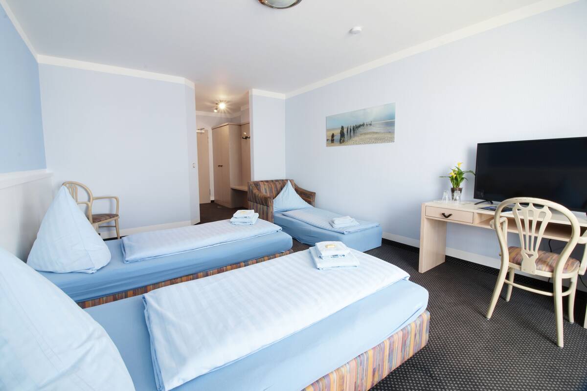 Een hotelkamer met twee bedden, een bureau, een stoel, een televisie en een schilderij aan de muur.