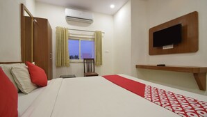 Une chambre d’hôtel équipée d’un lit, d’un téléviseur fixé au mur, d’une fenêtre avec des rideaux et d’un appareil de climatisation.