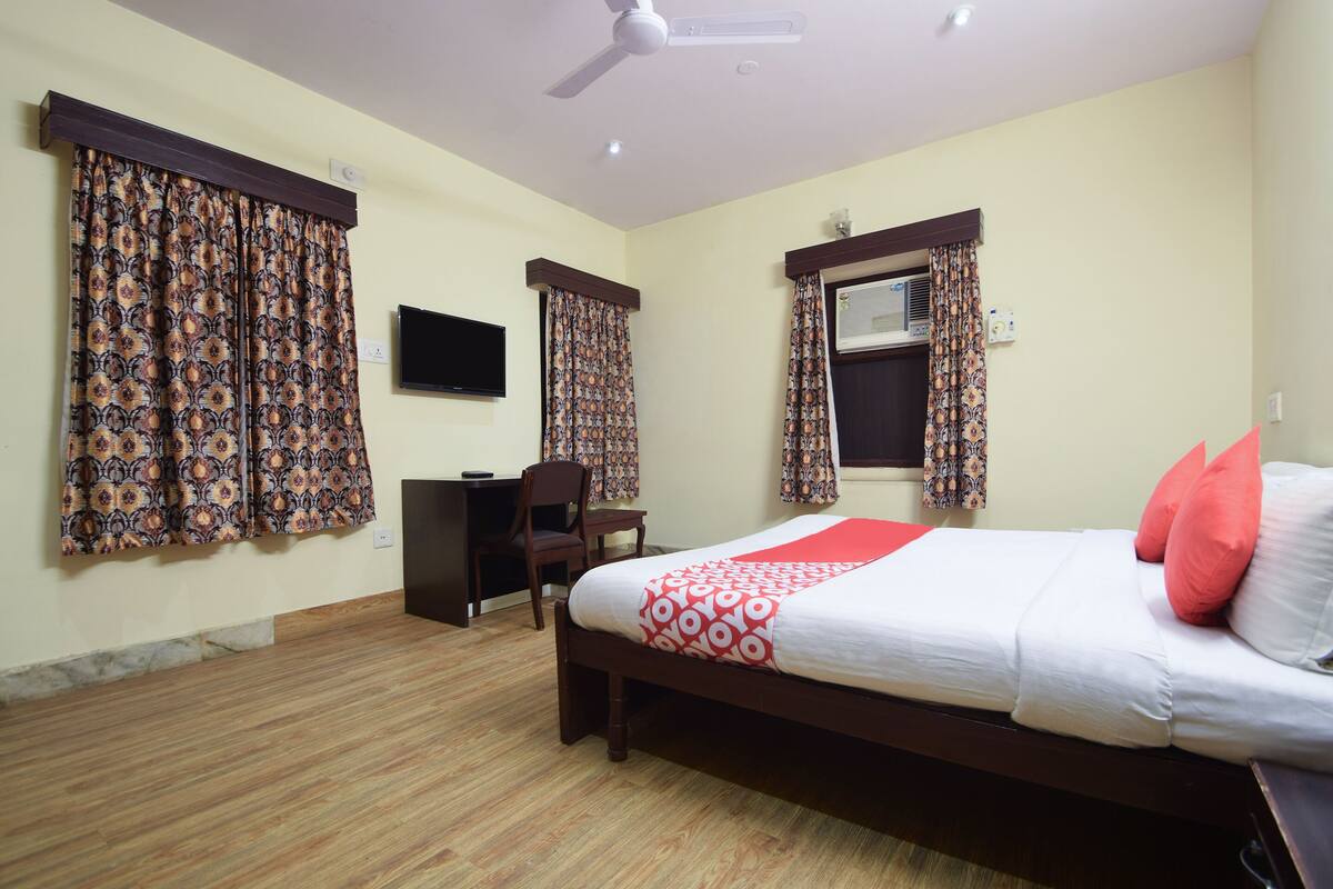 Une chambre d’hôtel avec un lit, un bureau, une chaise et un téléviseur fixé au mur.