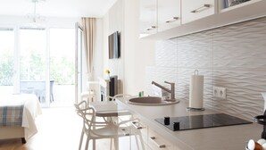 A modern kitchen with white cabinets, a central island, and a dining area with white chairs. - Sofie Apartments (Vienna)