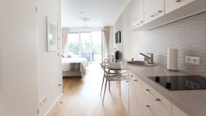 A modern kitchen with a dining area, a bed, and a view of greenery outside. - Sofie Apartments (Vienna)
