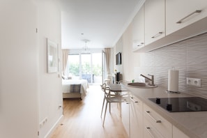 A modern kitchen with a dining area, a bed, and a view of greenery outside.