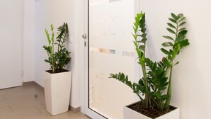 A modern hallway with a white door, two potted plants, a welcome mat, and a sign indicating A&A Apartments. - Sofie Apartments (Vienna)