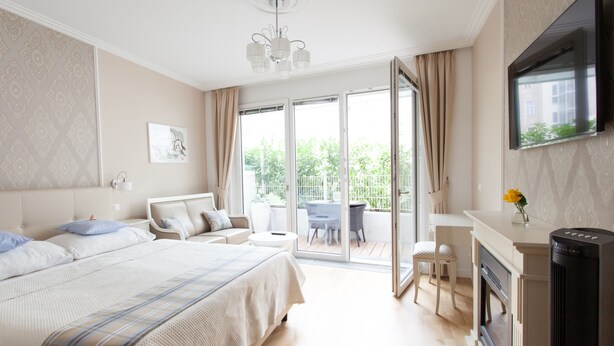 A bedroom with a bed, a TV, a fireplace, and a balcony with a table and chairs. - Sofie Apartments (Vienna)