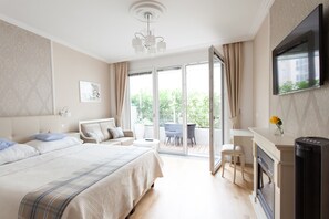 A bedroom with a bed, a TV, a fireplace, and a balcony with a table and chairs. - Sofie Apartments (Vienna)