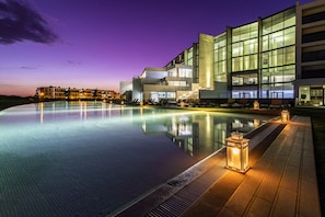 Ein modernes Hotel mit großem Infinity-Pool, Sitzgelegenheiten im Freien und einer gut beleuchteten Fassade.