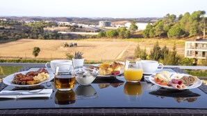 Een ontbijttafel met diverse gerechten, een kop thee en een glas sinaasappelsap, op een balkon met een mooi uitzicht.