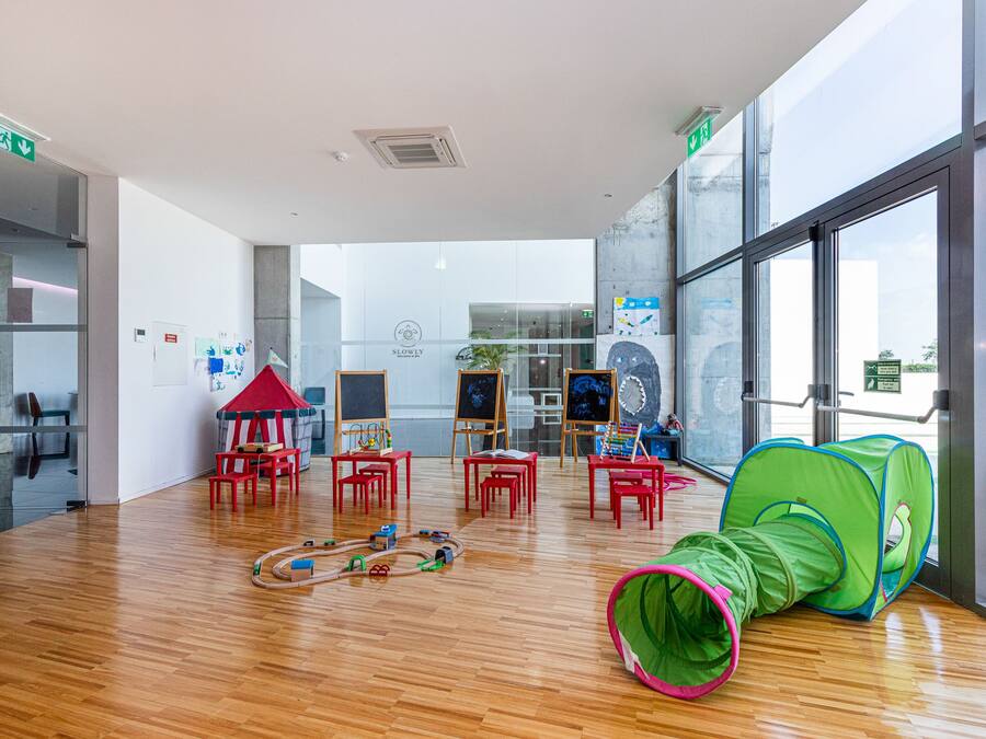 Una habitación amplia con piso de madera, sillas rojas, una tienda de juegos verde y una casita roja.