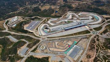 Une vue aérienne d’un vaste circuit automobile complexe, doté de nombreuses boucles et virages, et entouré d’une végétation clairsemée et de collines.