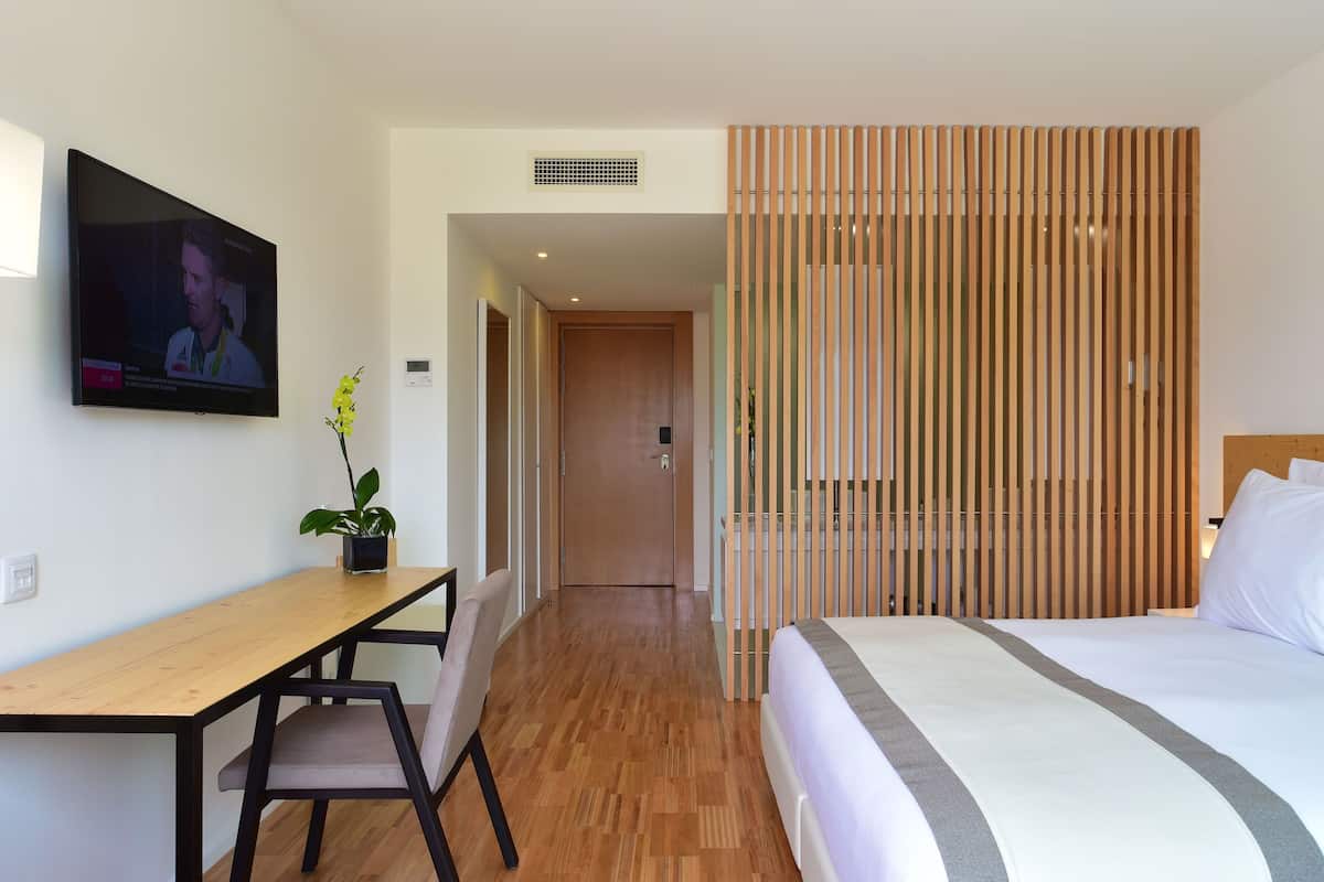 Hotelkamer met een houten bureau, een bed met witte beddengoed, een televisie aan de muur en een schuifdeur.
