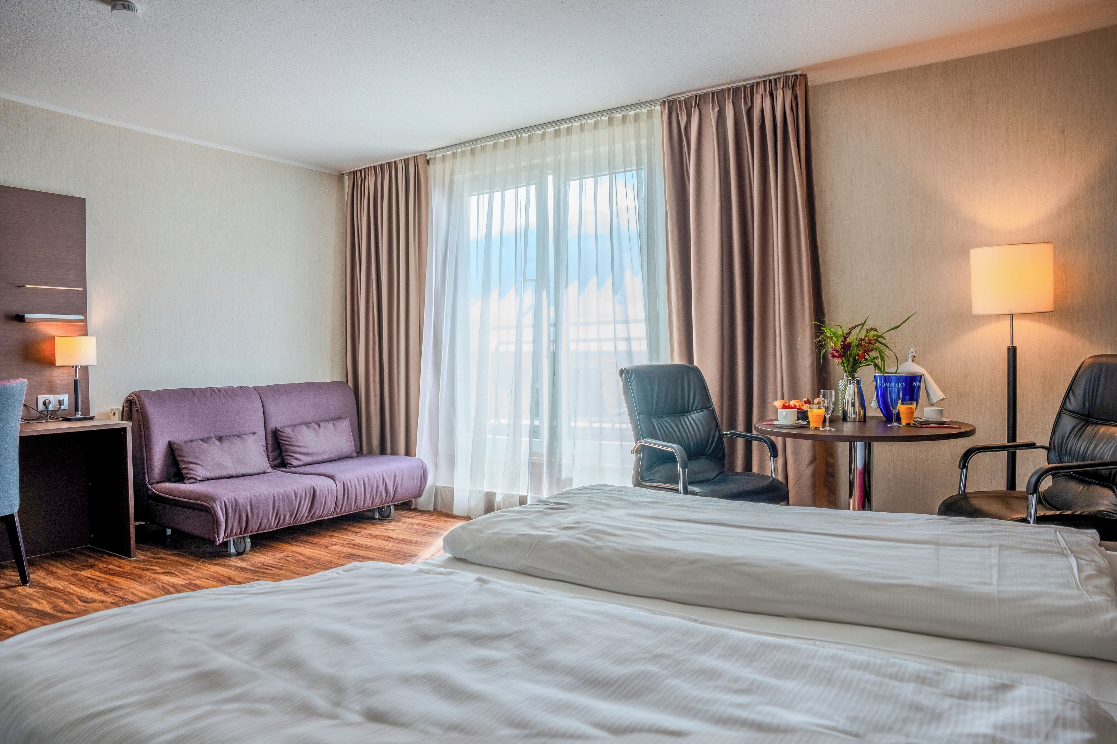 Une chambre d’hôtel comprenant un lit, un canapé, un bureau, une chaise et une petite table avec une lampe et une plante.