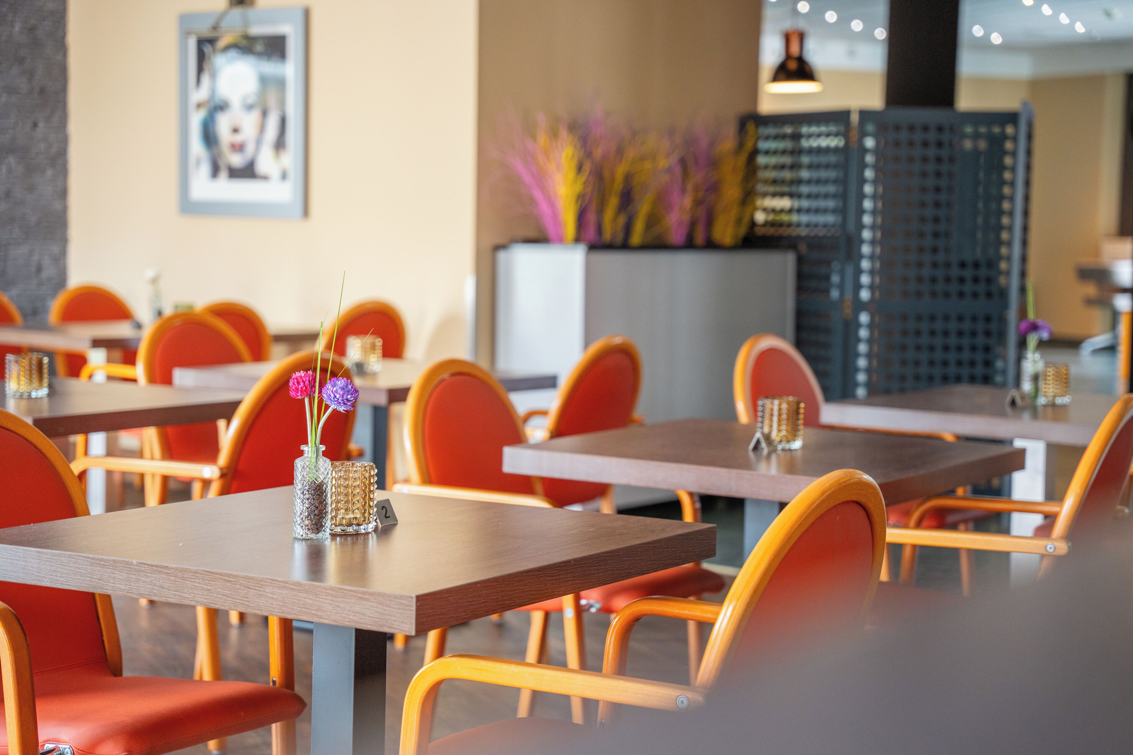 A restaurant interior with multiple tables and chairs, a decorative vase with flowers, and a framed picture on the wall.