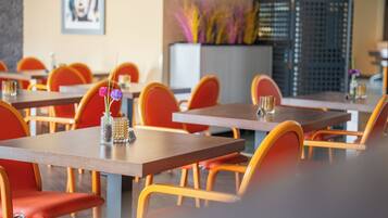 A restaurant interior with multiple tables and chairs, a decorative vase with flowers, and a framed picture on the wall.