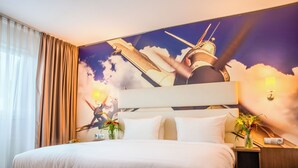 Ein Hotelzimmer mit einem großen Bett, einem Vorhang mit Wandgemälde, einem Nachttisch mit Lampe und einer Vase mit Blumen.