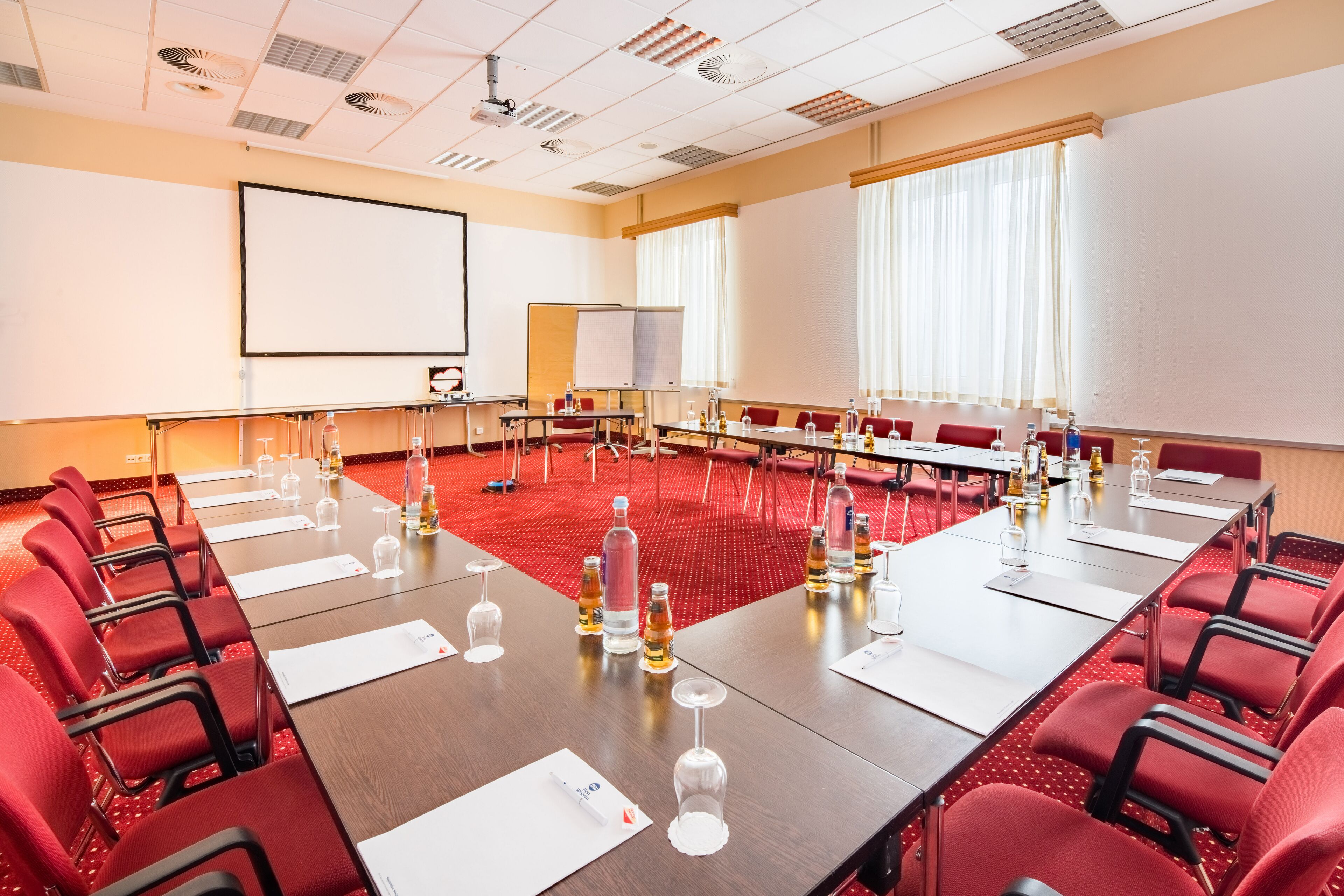 A conference room with a long table, red chairs, a projector screen, and a whiteboard.