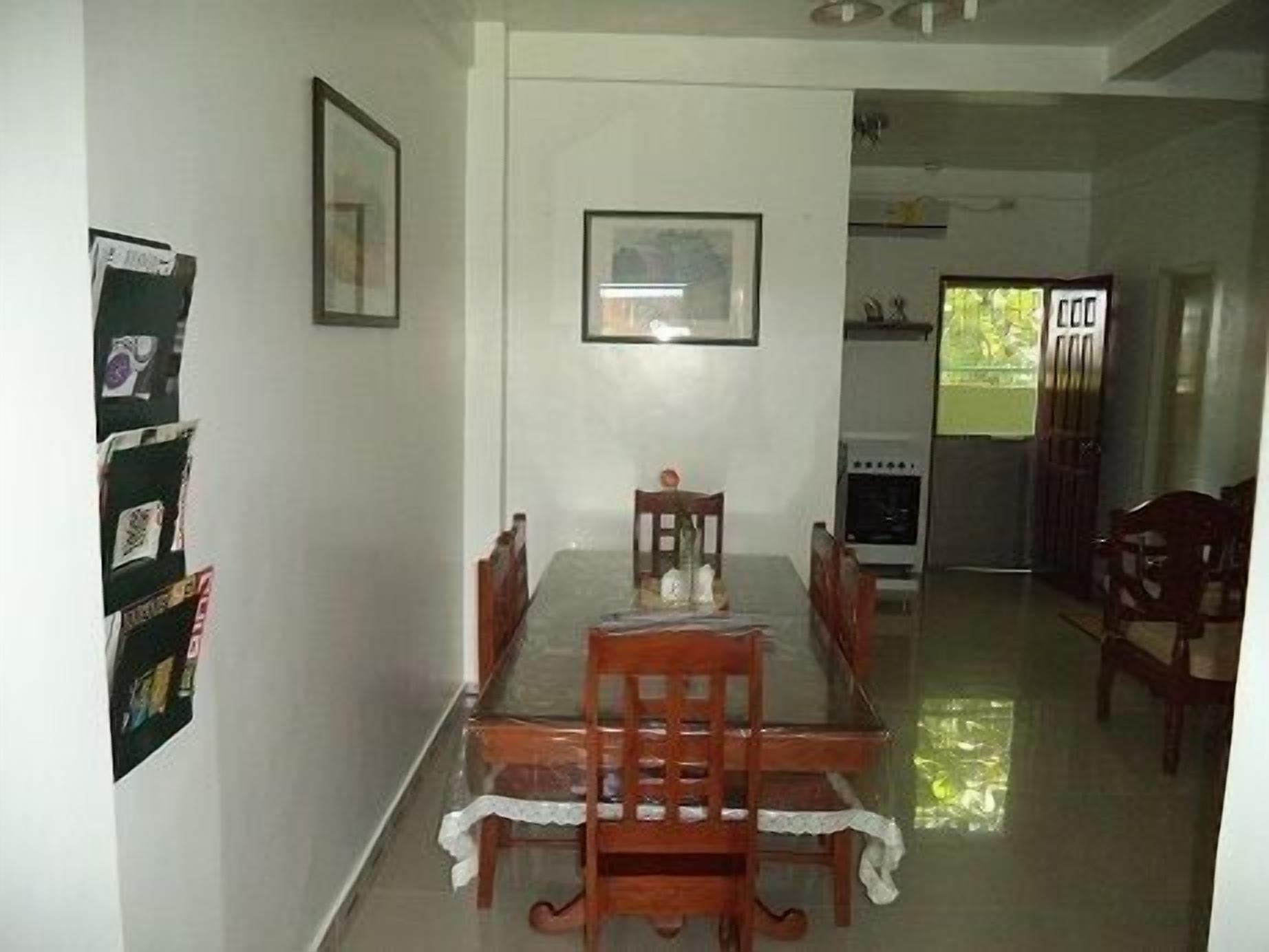 Uma área de refeições com mesa, cadeiras, geladeira e janela com luz natural.