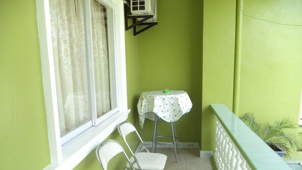 Un pequeño balcón con una mesa y sillas, una ventana con cortinas y una pared verde.