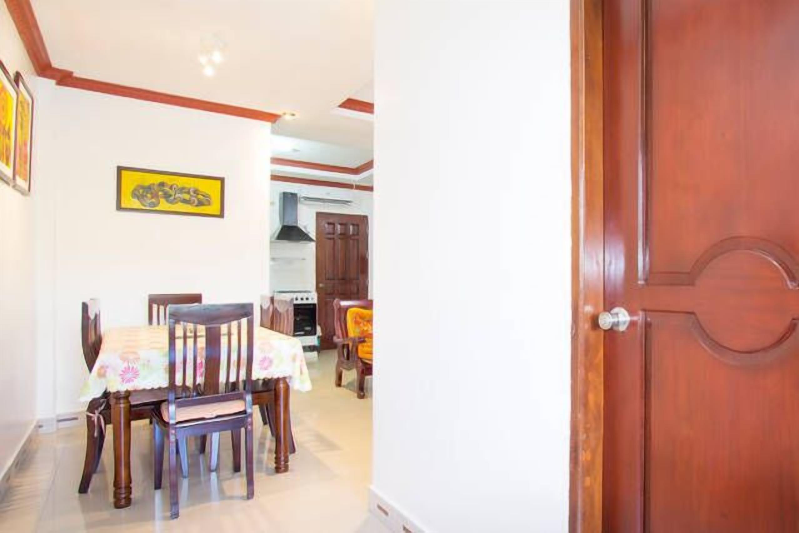 A dining area with a table set for four, a wooden door, and a kitchen in the background.