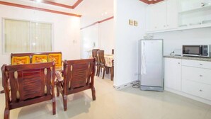 Un comedor con sillas de madera y una mesa, una cocina con armarios y electrodomésticos blancos, y un ventilador de techo.