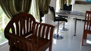 Una cocina moderna con armarios blancos, microondas y una zona de comedor con una silla de madera y un taburete alto.