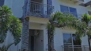 Un edificio residencial de varios pisos con balcones, una escalera central y palmeras circundantes.