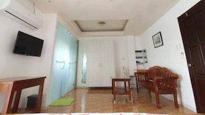 Una habitación con una televisión de pantalla plana montada en la pared, un banco de madera, una mesita pequeña y un tapete verde en el suelo.