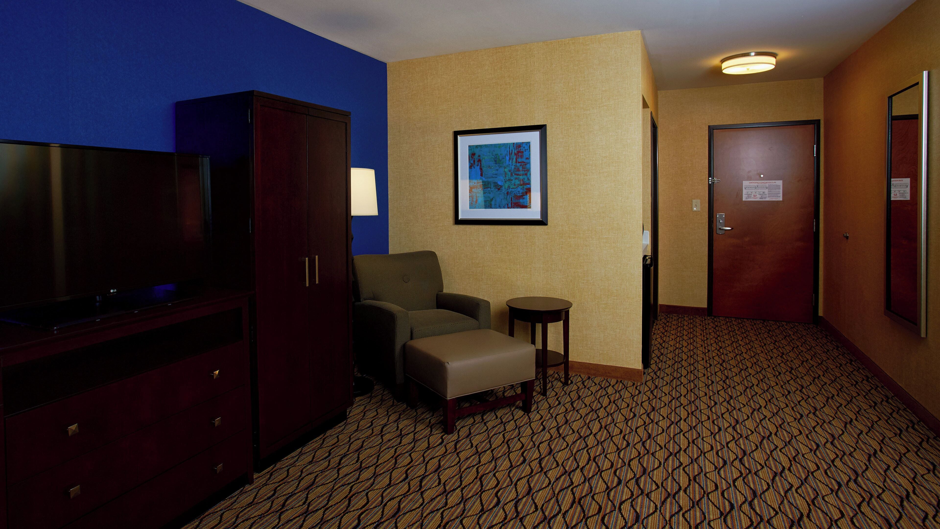 A hotel room with a television, a sofa, a small table, a framed picture on the wall, and a patterned carpet.