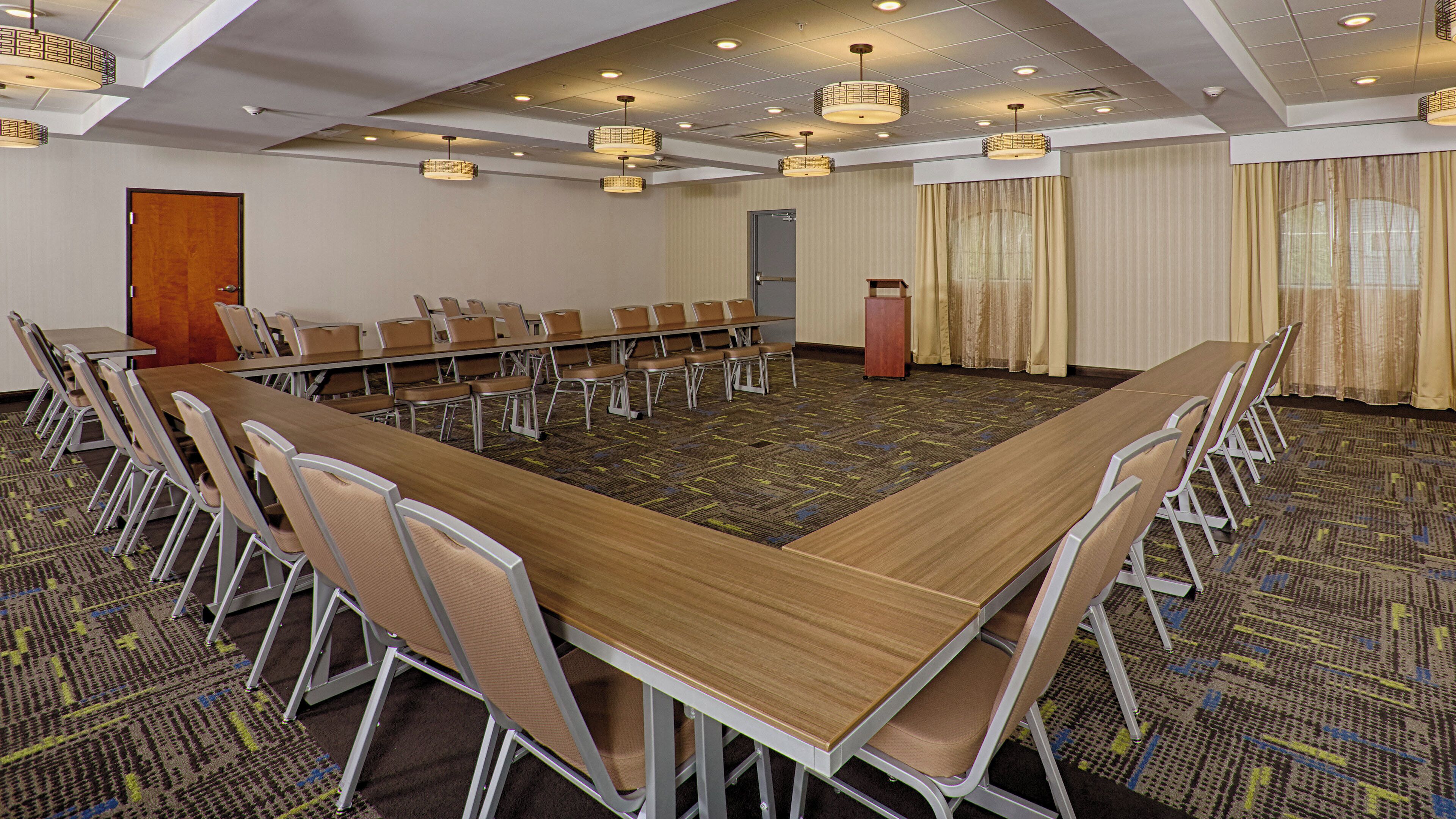 Une salle de conférence avec une longue table, des chaises, un pupitre et des rideaux.