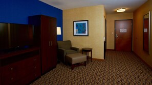 Een hotelkamer met een televisie, een bank, een klein tafeltje, een inlijsting afbeelding aan de muur en een kamerbreed tapijt.