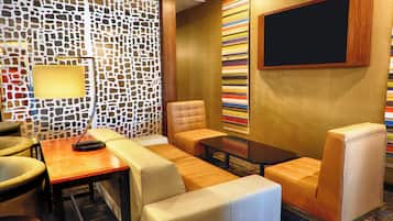 A modern lounge area with a sofa, armchairs, a coffee table, and a wall-mounted TV.