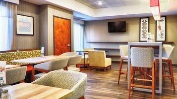 A hotel room with a dining area, a TV mounted on the wall, and a wooden floor.