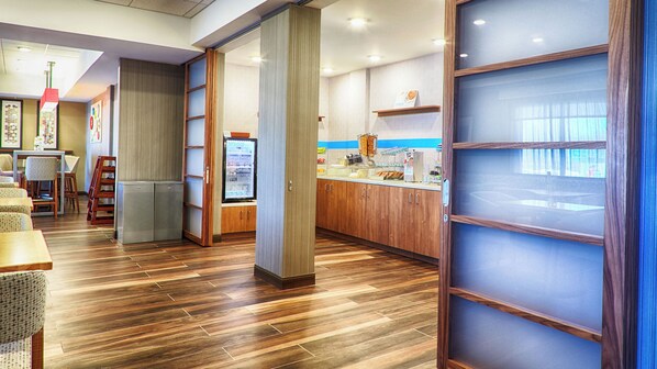 Un restaurante con piso de madera, una barra con exhibición de alimentos y un refrigerador.