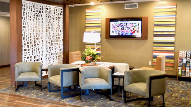 Un vestíbulo de hotel con una recepción, cuatro sillones, un televisor y un panel decorativo en la pared.