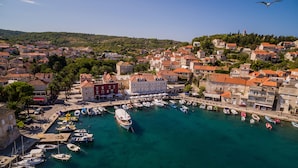 Une ville côtière dotée d’un port de plaisance rempli de bateaux, de bâtiments historiques aux toits recouverts de tuiles rouges et d’un ciel bleu azur.