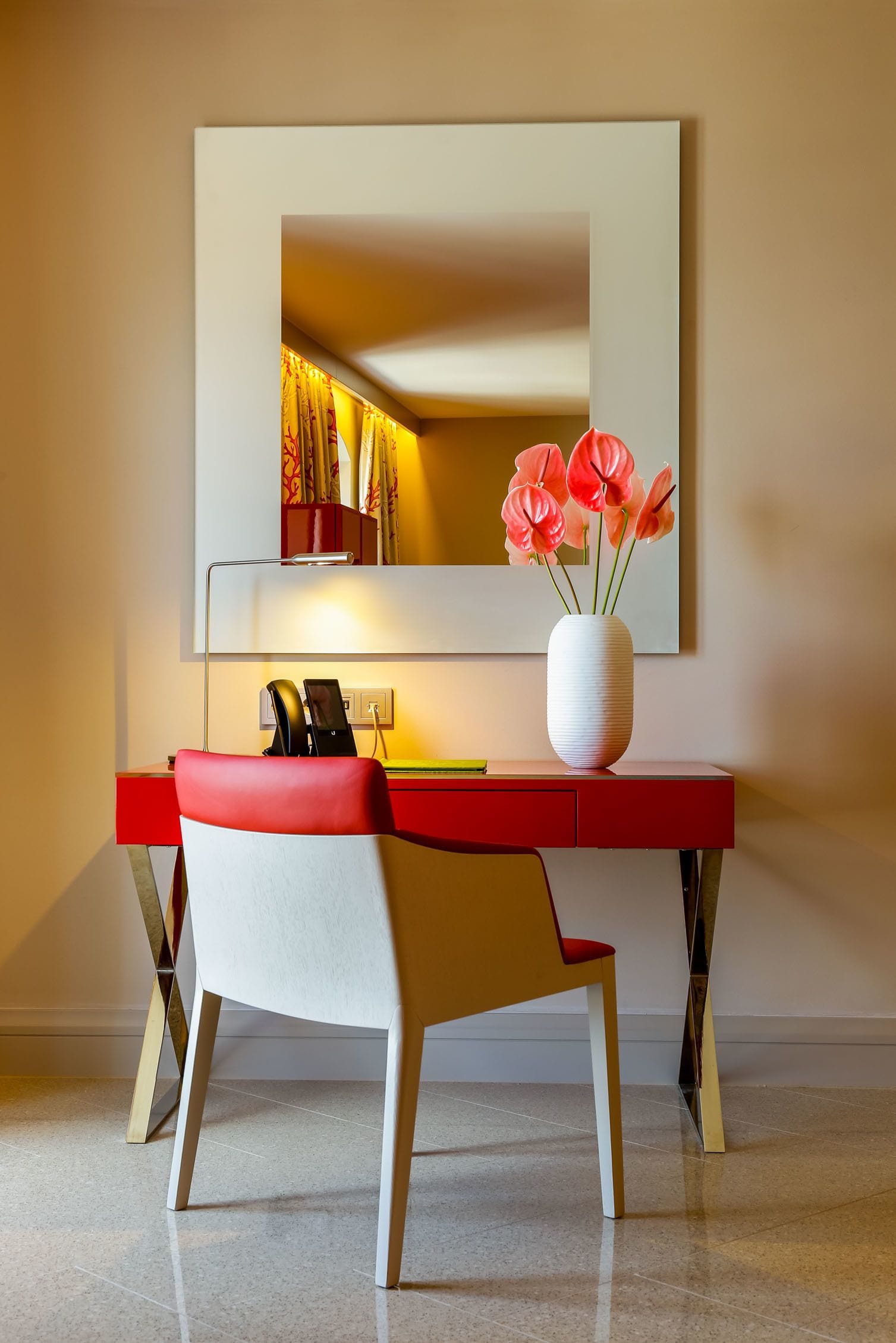 Un escritorio moderno con un jarrón de flores, una silla y un espejo en la pared.