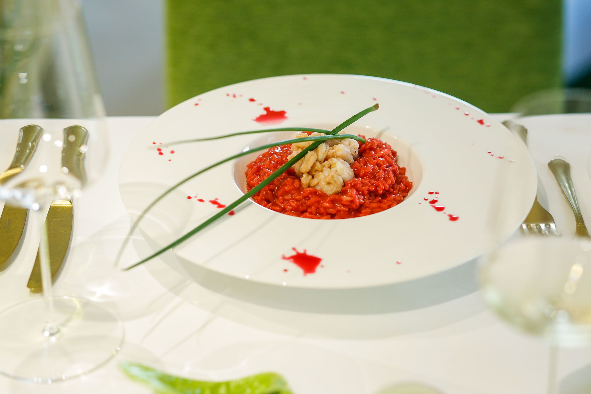 A white plate with red sauce and garnish on a table with white tableware.