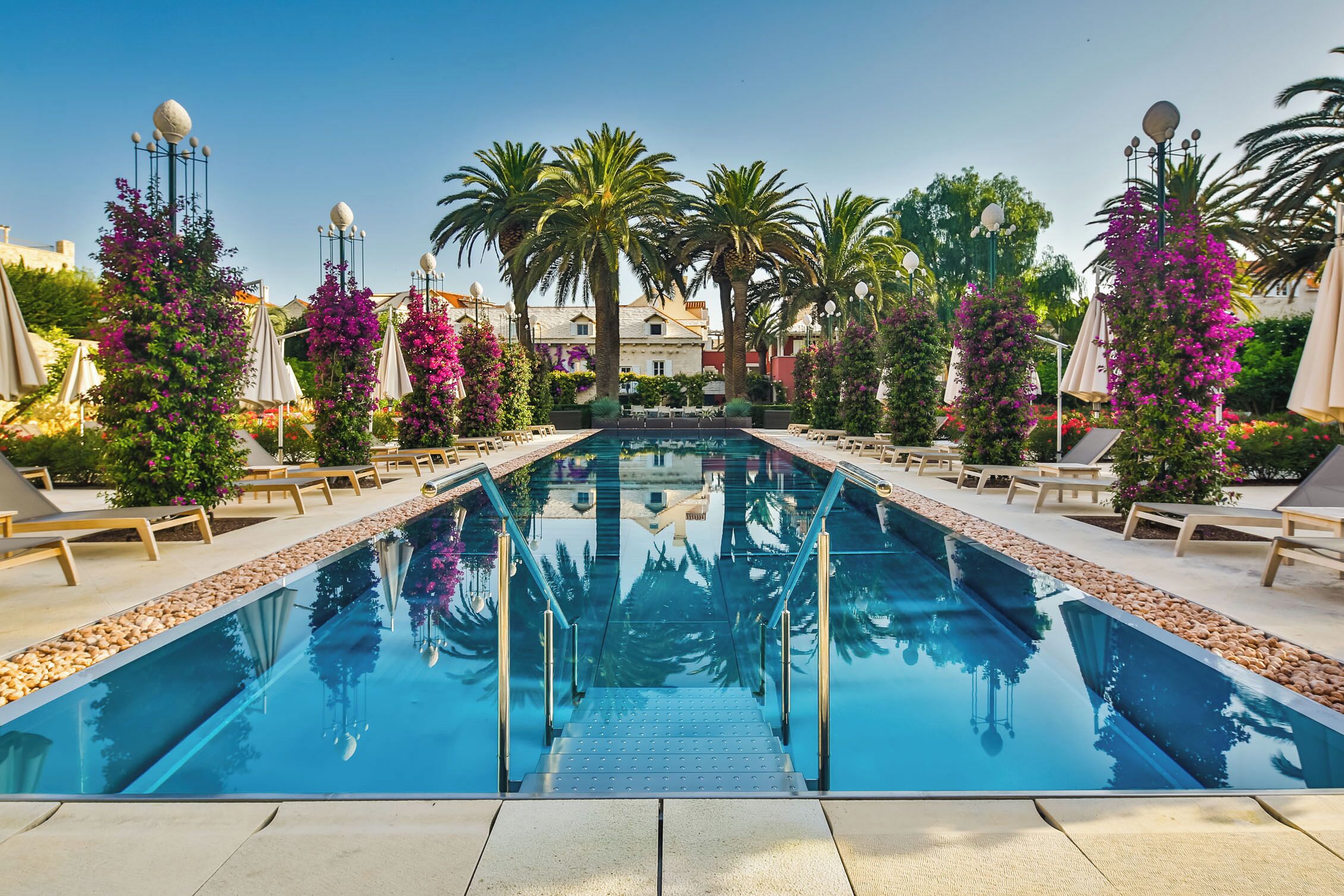 A swimming pool with a clear view of the water, surrounded by lounge chairs and palm trees.