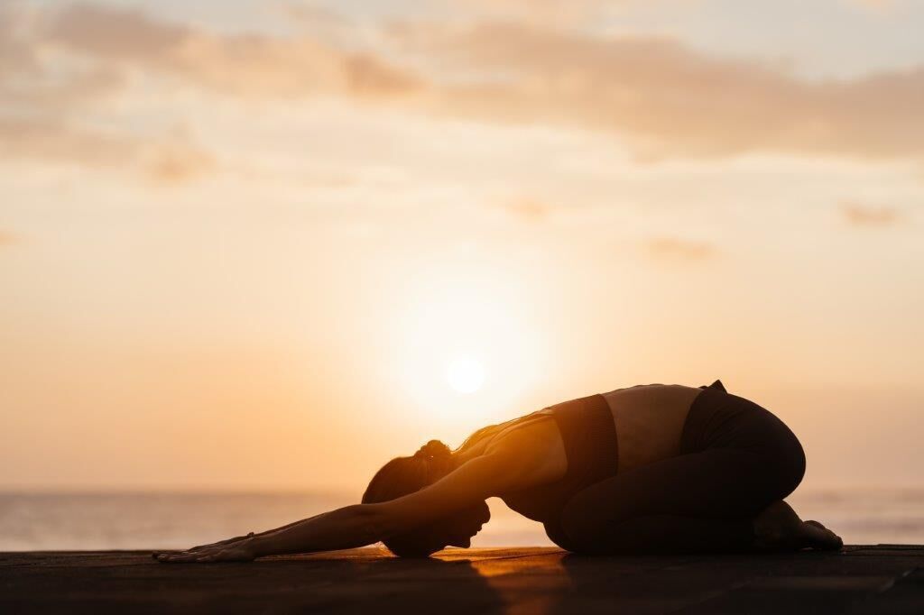 A person in a yoga pose on a beach at sunset.