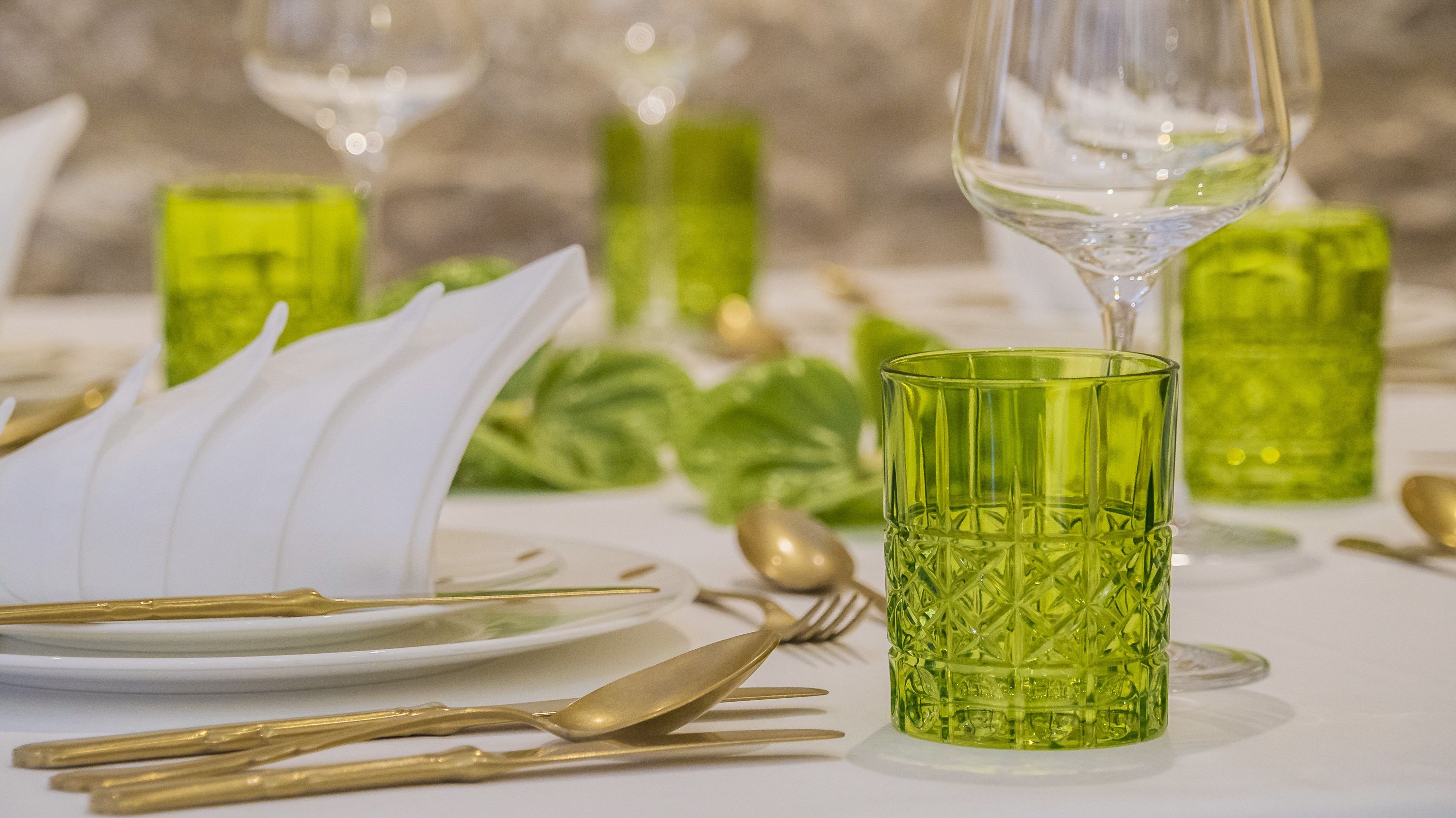 Une table dressée avec de la verrerie verte, des couverts dorés et des serviettes blanches.
