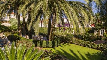 A well-maintained garden with palm trees, a neatly trimmed lawn, and a dining area with tables and chairs.