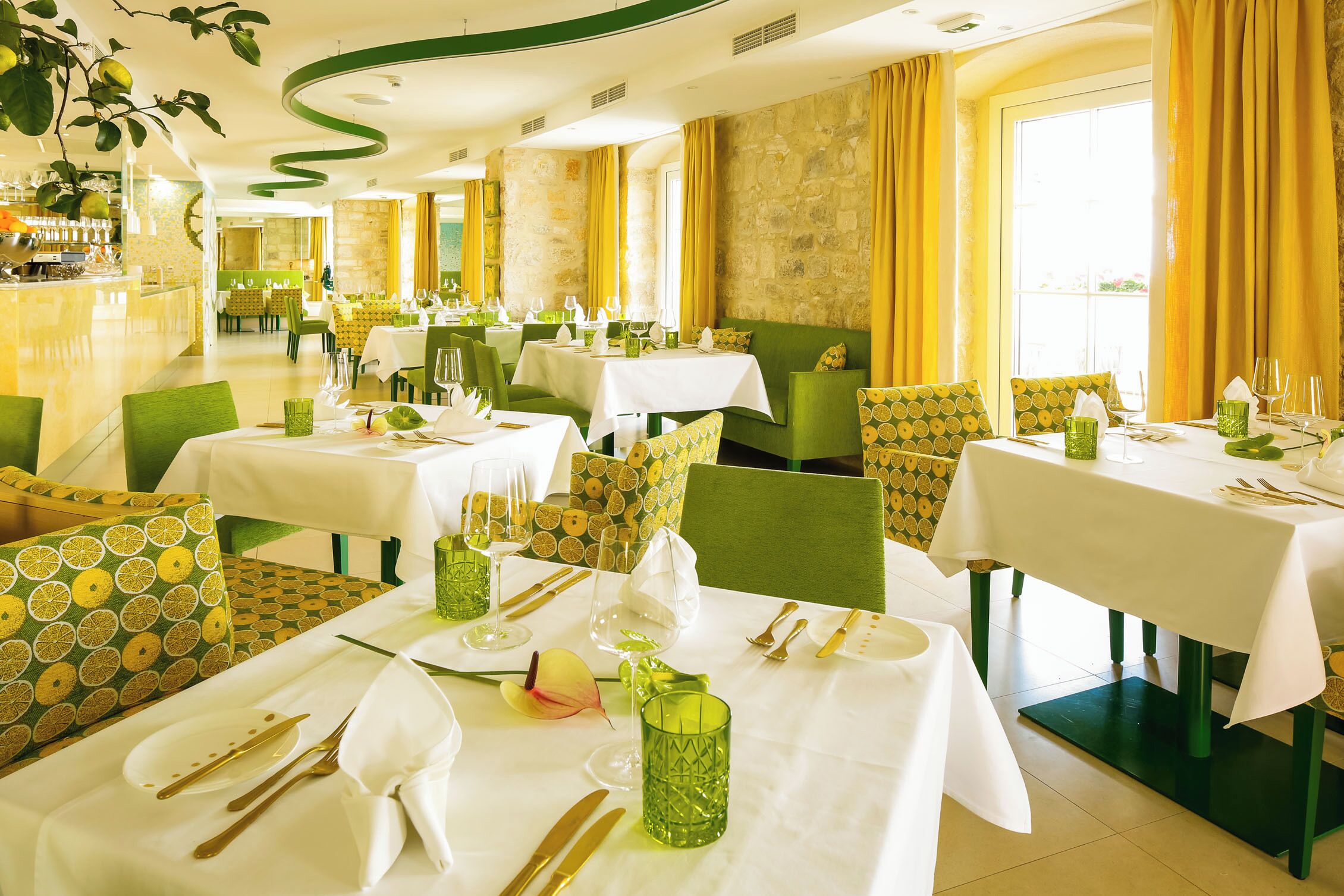 A restaurant with multiple tables set for dining, featuring green chairs and white tablecloths.